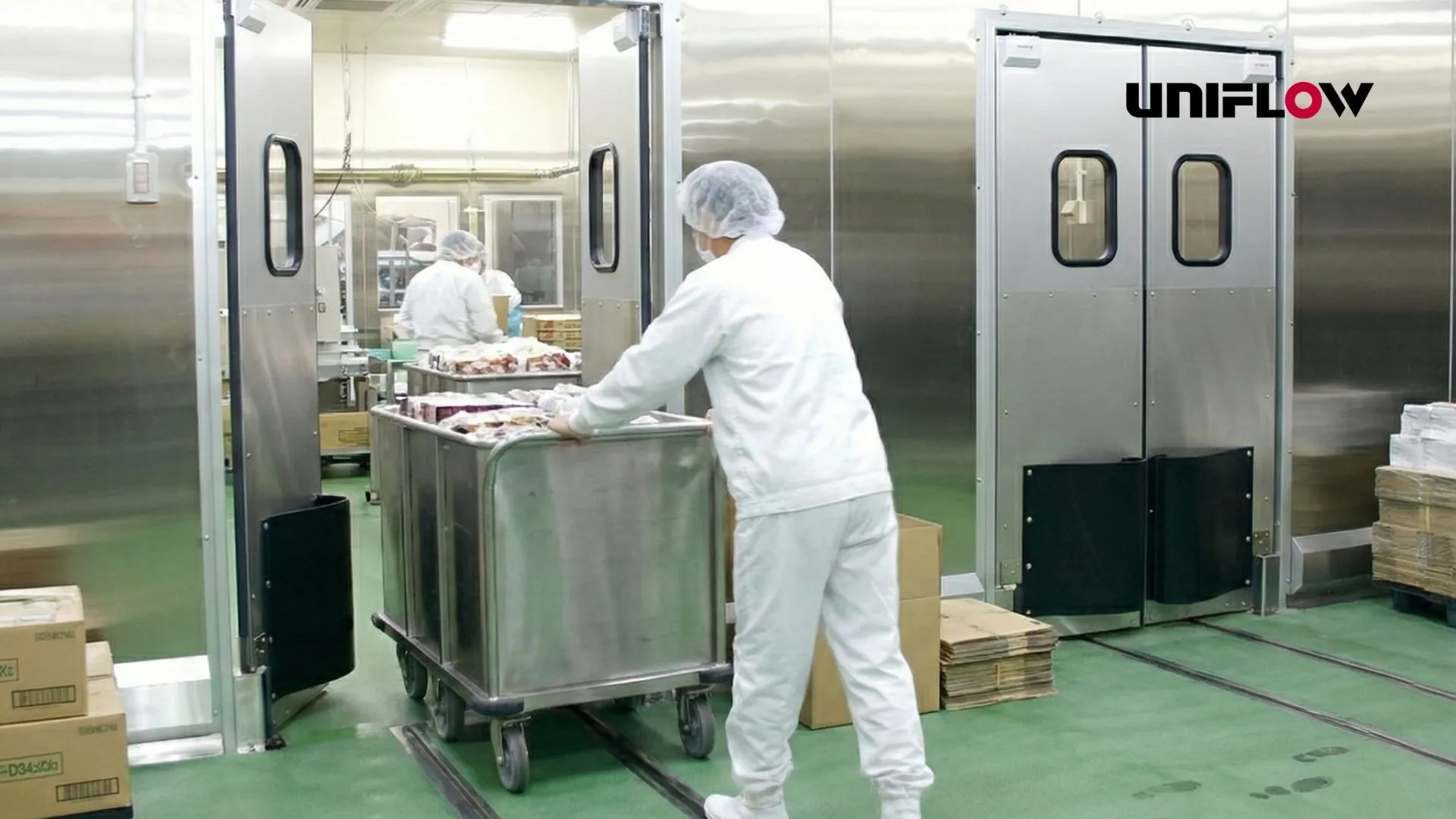 Pintu swing door dengan karyawan sedang melewatinya dengan membawa bahan makanan dengan logo uniflow di sebelah kanan atas.